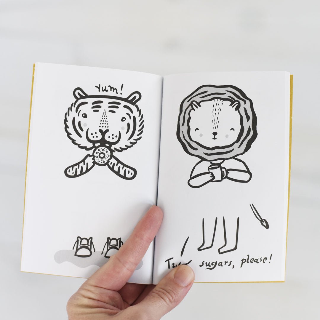 Illustrated book open to pages with a tiger and a lion, held by a hand.